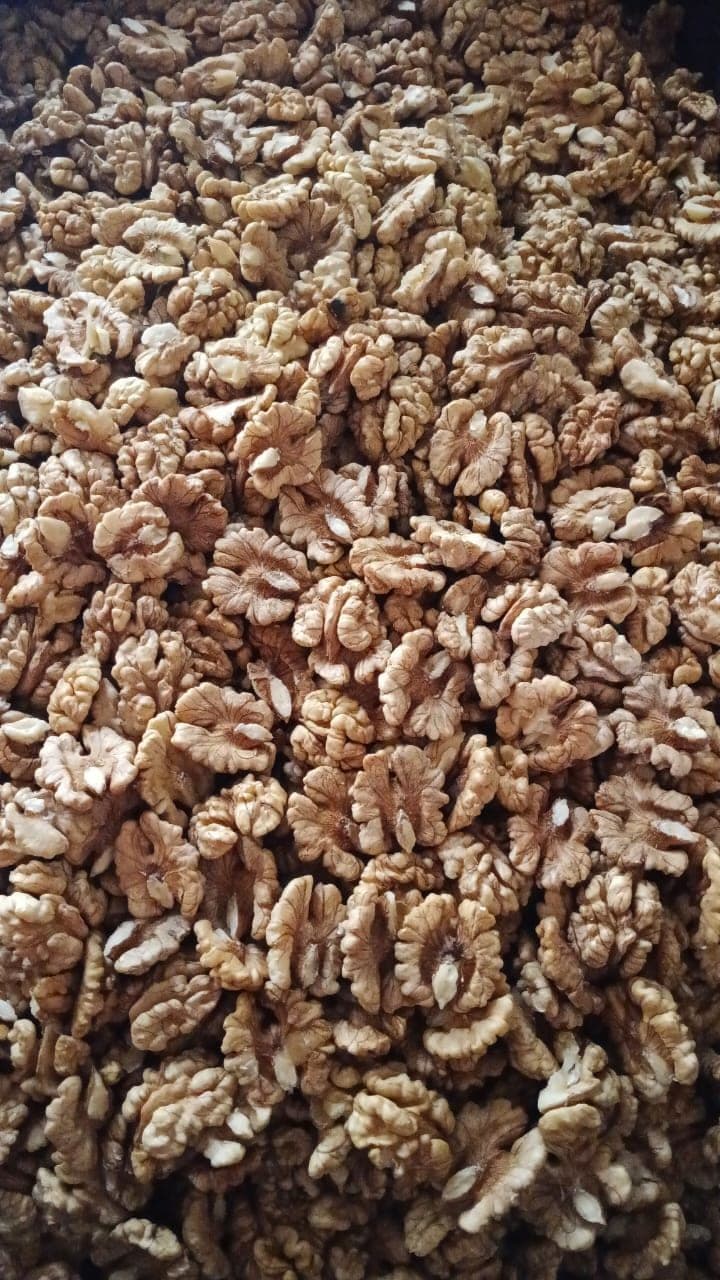A deep bulk pile of pale walnut halves filling the frame, sizes and shades varying kernel to kernel