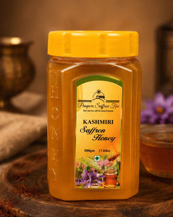 A 500 g yellow-capped jar of Kashmiri Saffron Honey on a wooden board, a bowl of honey and saffron threads behind