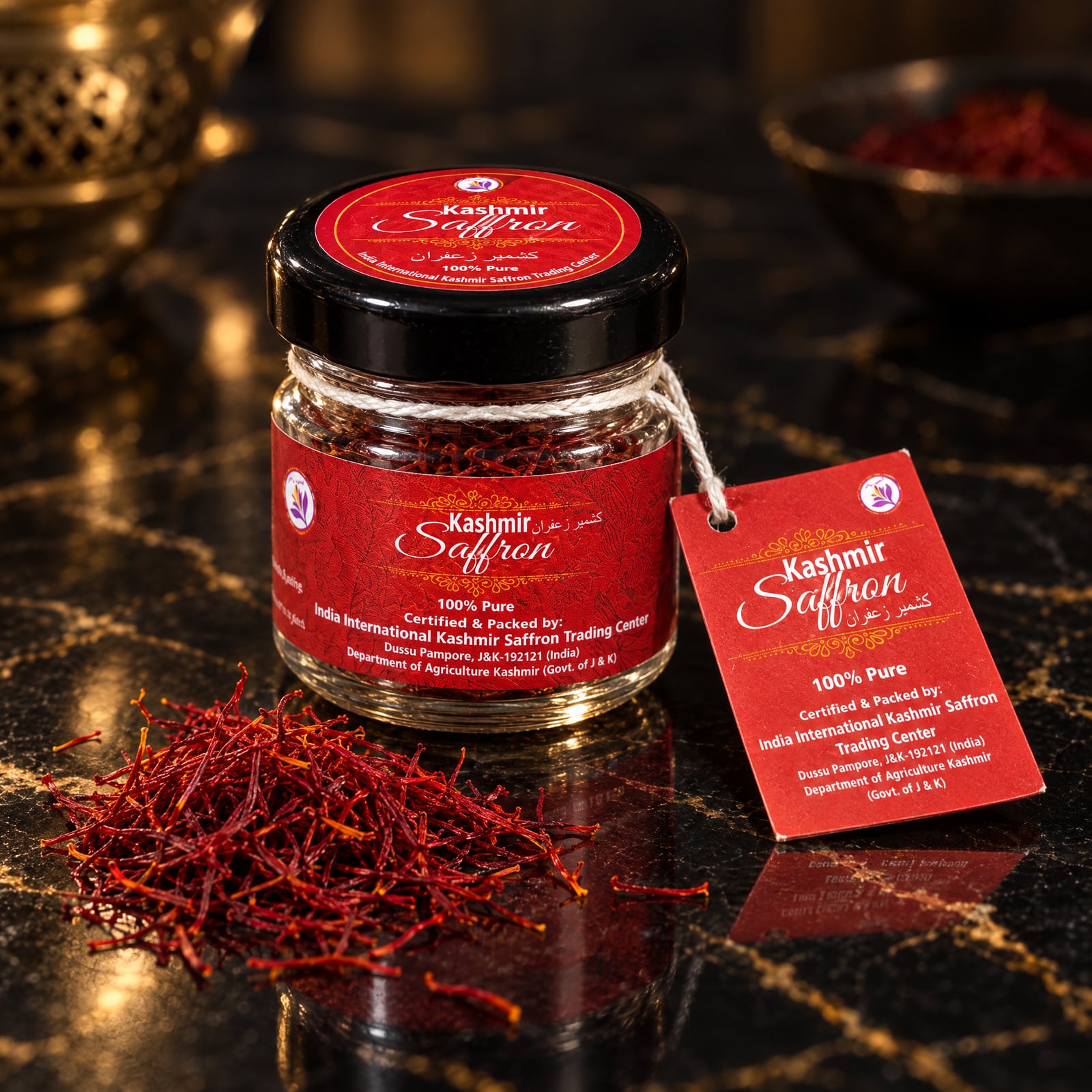 The IIKSTC Kashmir Saffron jar on black marble with a loose pinch of crimson saffron threads in front and the red hang tag lying beside it