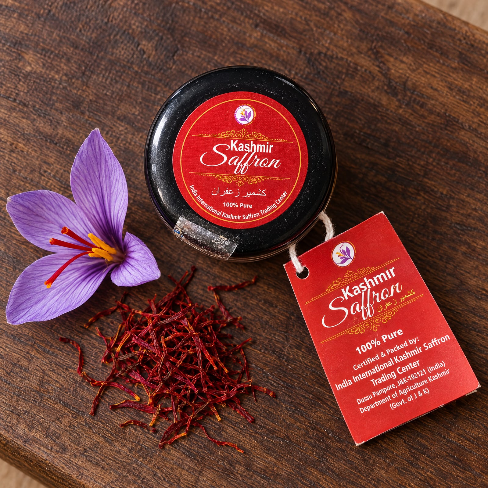 Looking down at the jar's black lid and round red Kashmir Saffron label on a walnut board, beside a purple crocus flower, loose threads and the tag