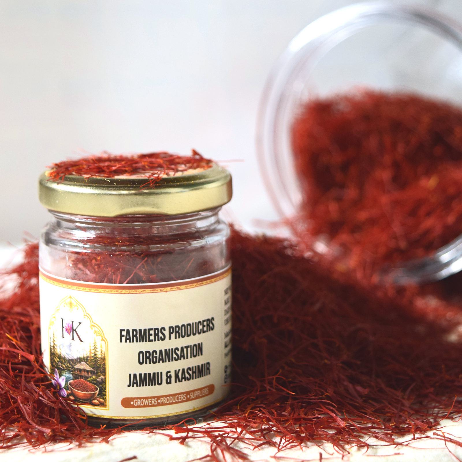 The saffron jar's label reading Farmers Producers Organisation Jammu & Kashmir, the jar set in a drift of red saffron threads