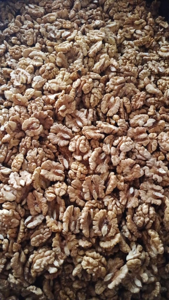 A deep bulk pile of pale walnut halves filling the frame, sizes and shades varying kernel to kernel