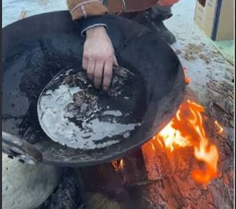 Shilajit resin being cooked in a blackened pan over an open wood fire