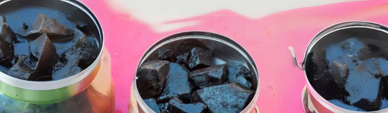 Buckets of dark shilajit resin lined up on a pink surface during purification