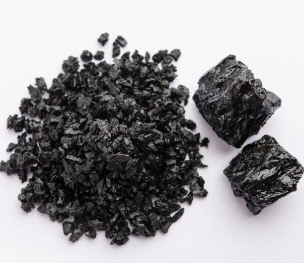 Chunks of black shilajit resin piled on a white background beside unbroken lumps