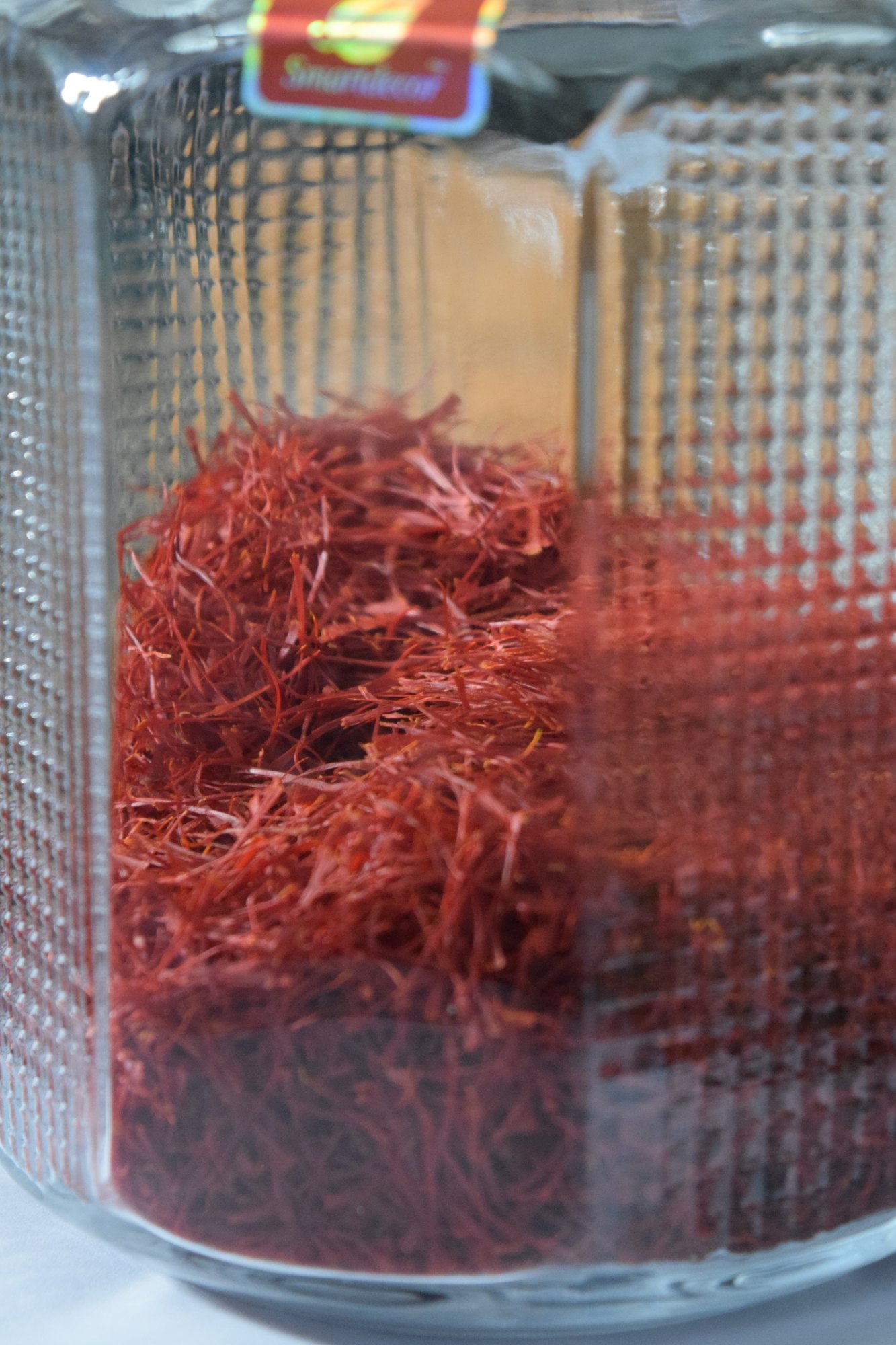 Red saffron threads packed inside a ribbed glass jar, seen close up through the glass