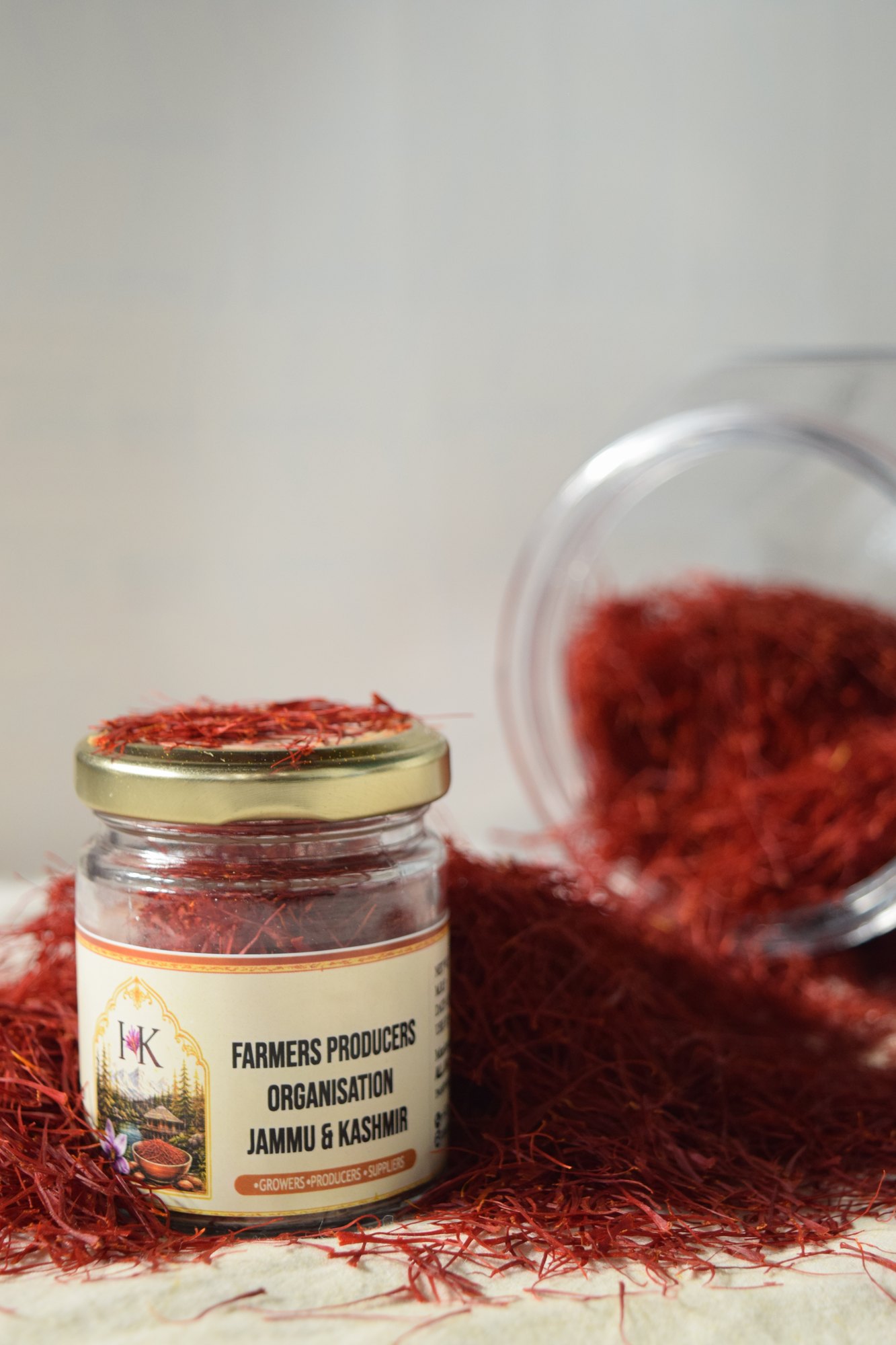 A gold-lidded saffron jar with its label facing forward, surrounded by loose red saffron threads