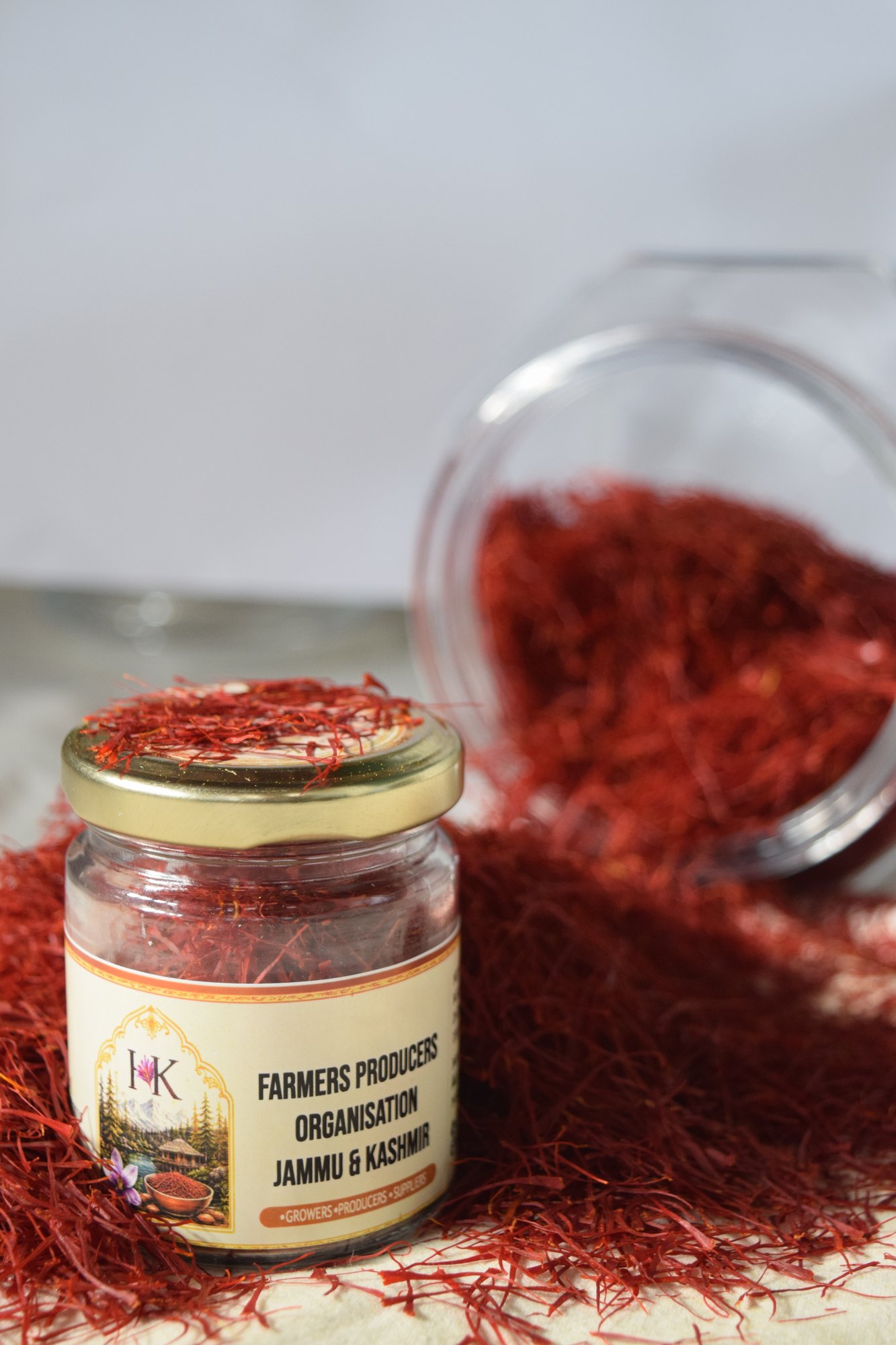 A small labelled jar of saffron standing in a heap of red threads, with a tipped glass jar behind