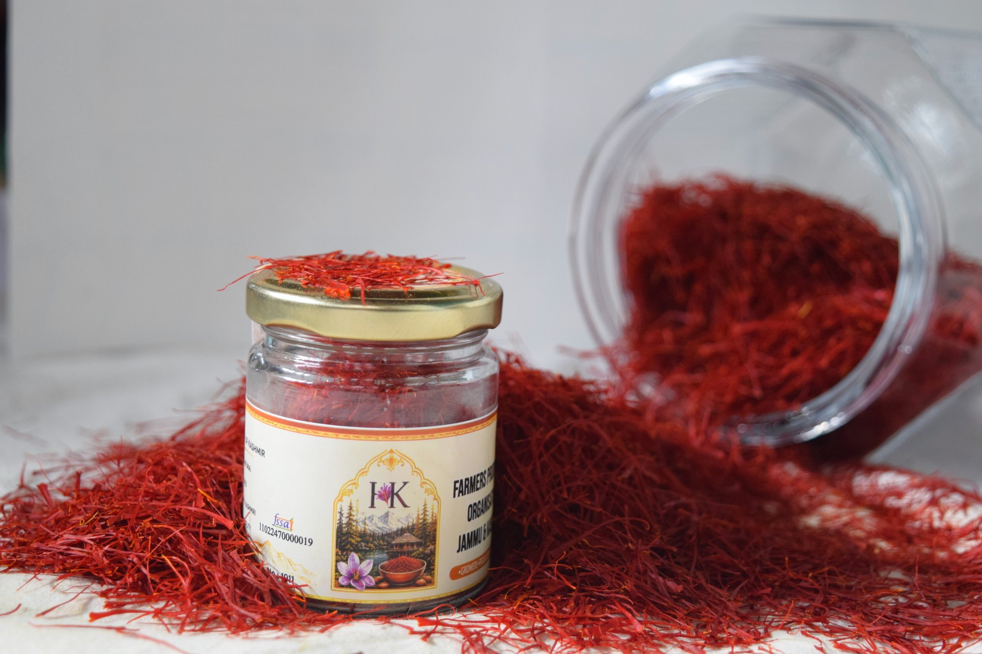 A labelled saffron jar on a bed of loose red threads, a glass jar lying on its side behind it